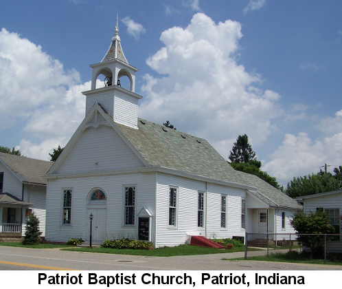 Color photograph of a traditional white clapboard church with a stubby steeple and an arched window over the double main-entrance doors